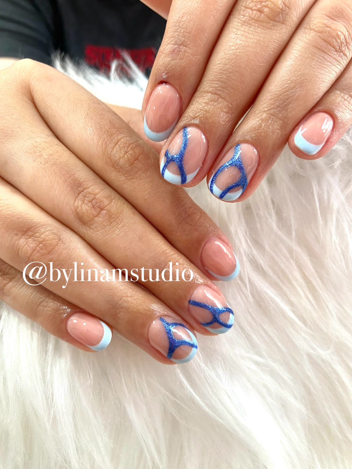 Manicura ovalada nude con francesa azul celeste y líneas azules brillantes