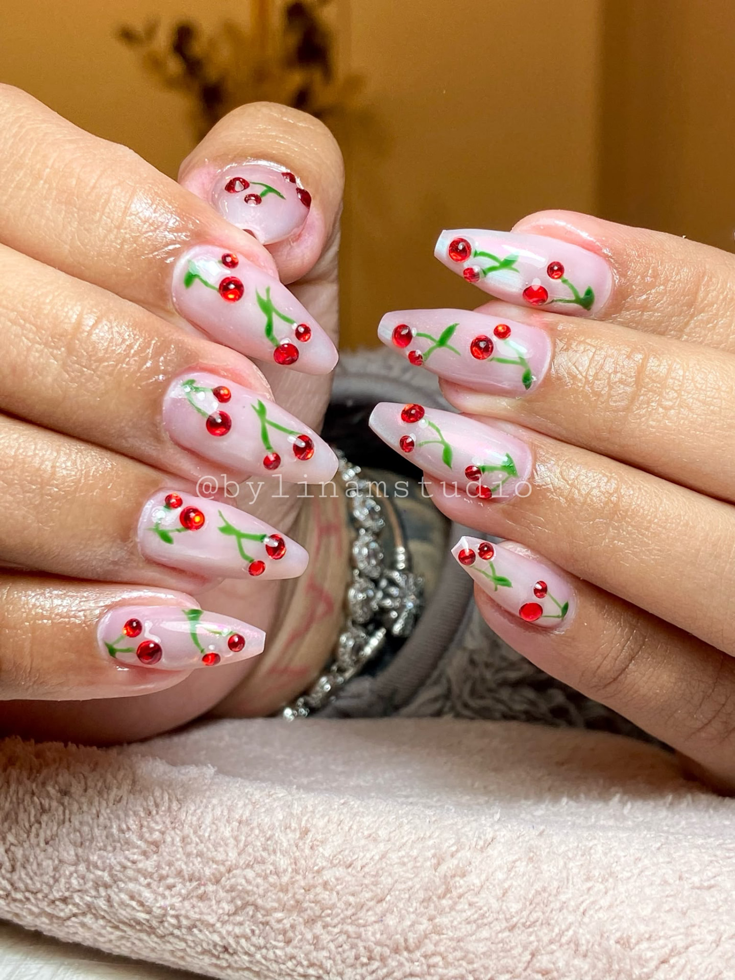 Manicura ballerina lechosa con cerezas en pedrería roja y hojas pintadas en verde