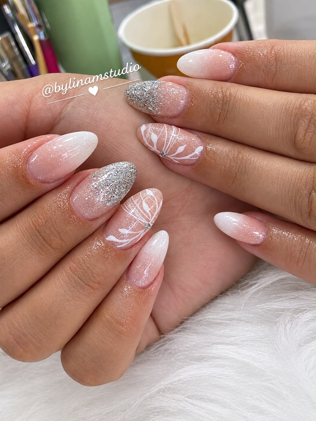 Manicura almendrada nude con degradado blanco, purpurina plateada y detalles botánicos