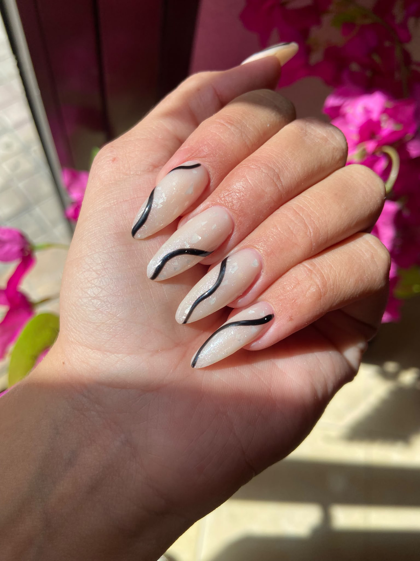 Manicura almendrada larga en blanco perla con destellos y líneas onduladas negras